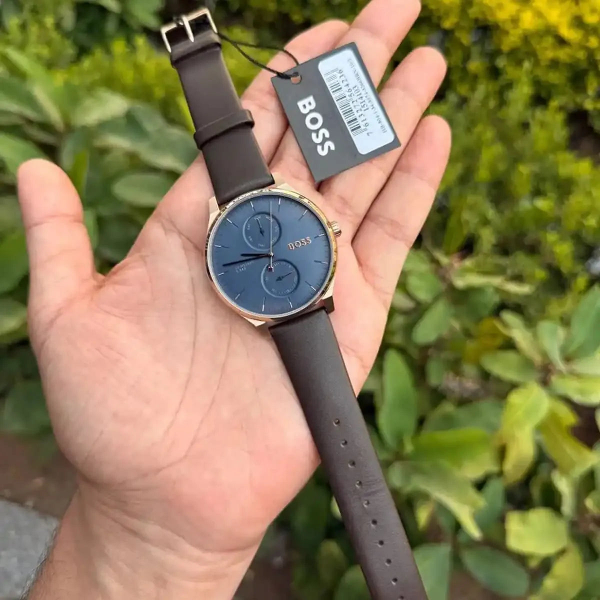 Hugo Boss Tyler quartz watch held in hand with product tag, blue dial and brown leather strap visible