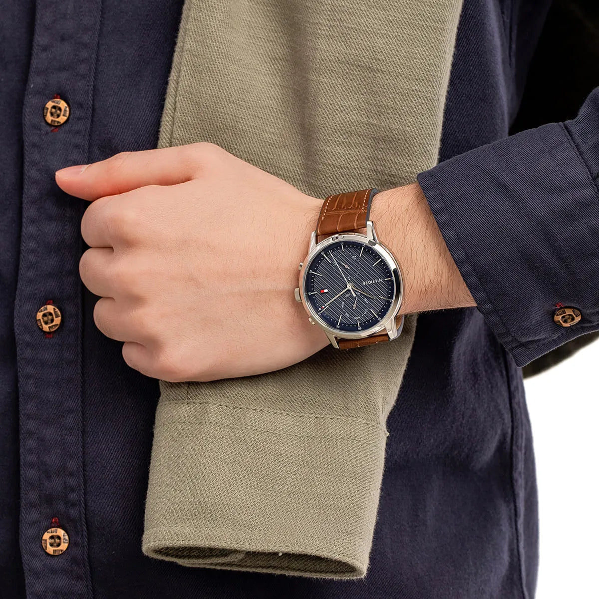 Watch worn on wrist with navy blazer showing brown leather strap and dial