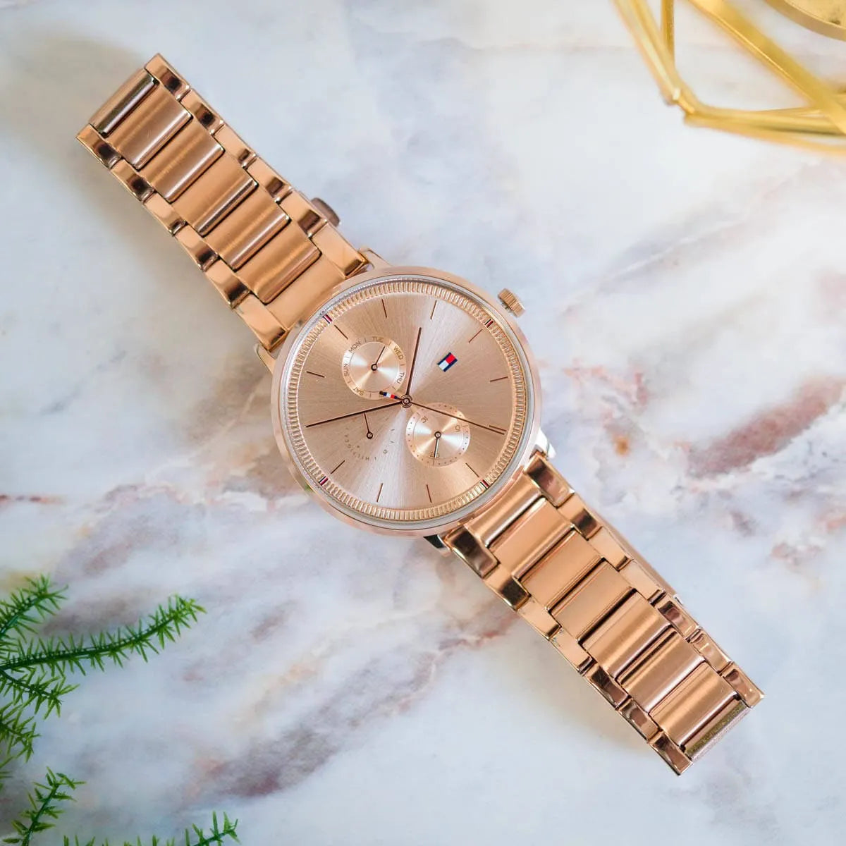 Flat lay of rose gold Tommy Hilfiger women's watch with multifunction chronograph dial on marble background