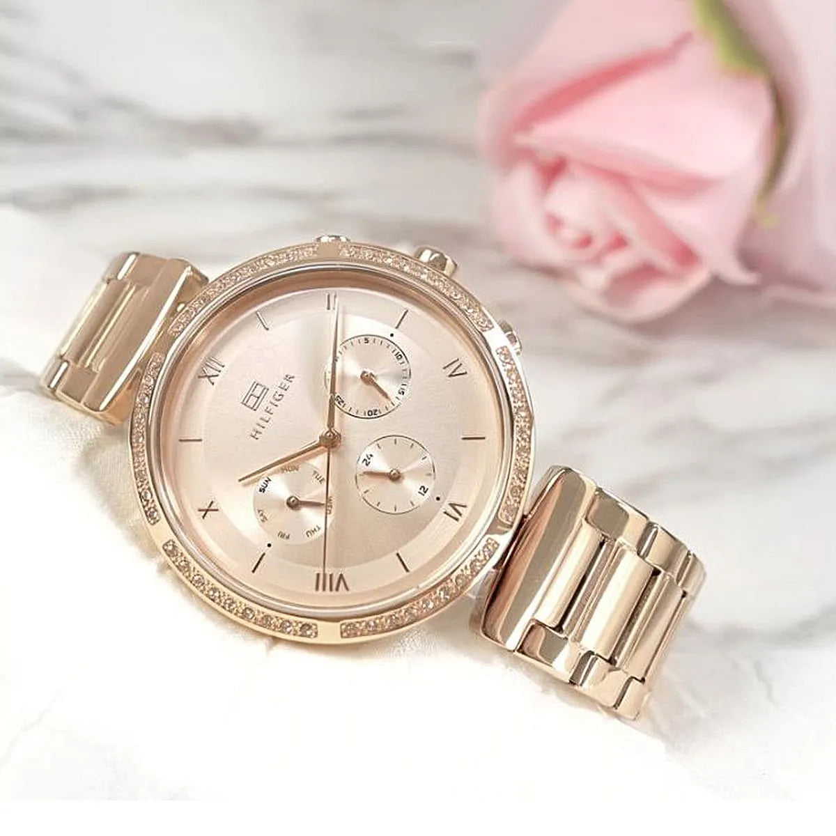 Tommy Hilfiger rose gold women's watch worn on wrist with pink background