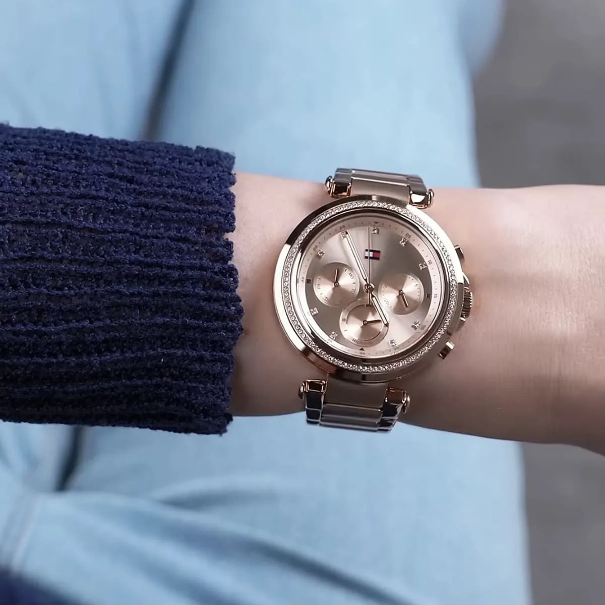 Rose gold women's chronograph watch worn on wrist with navy knit sleeve