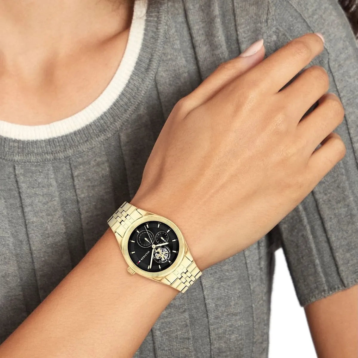 Tommy Hilfiger Monica gold watch on wrist with gray shirt and white long sleeve
