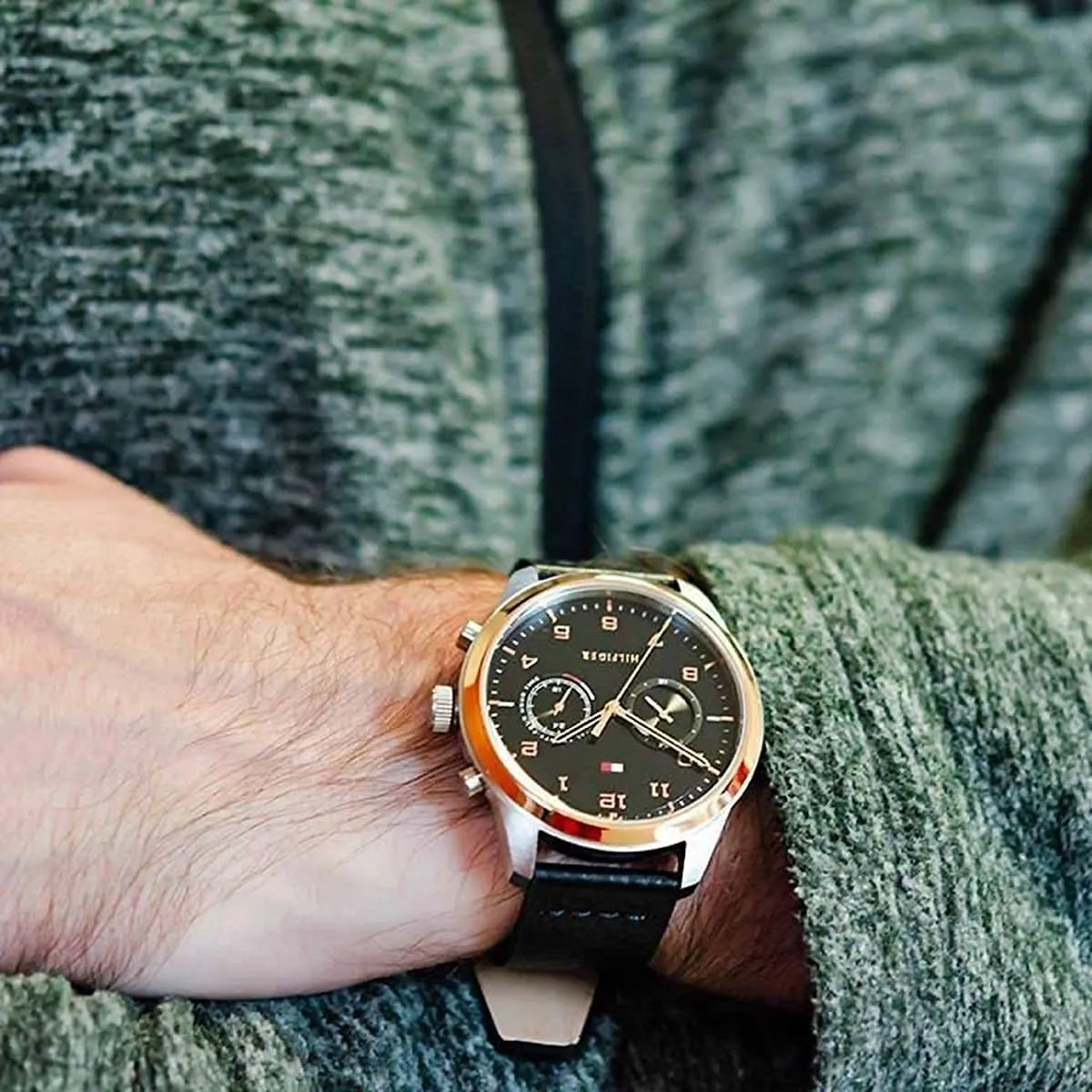 Tommy Hilfiger watch worn on wrist with black leather strap against green sleeve