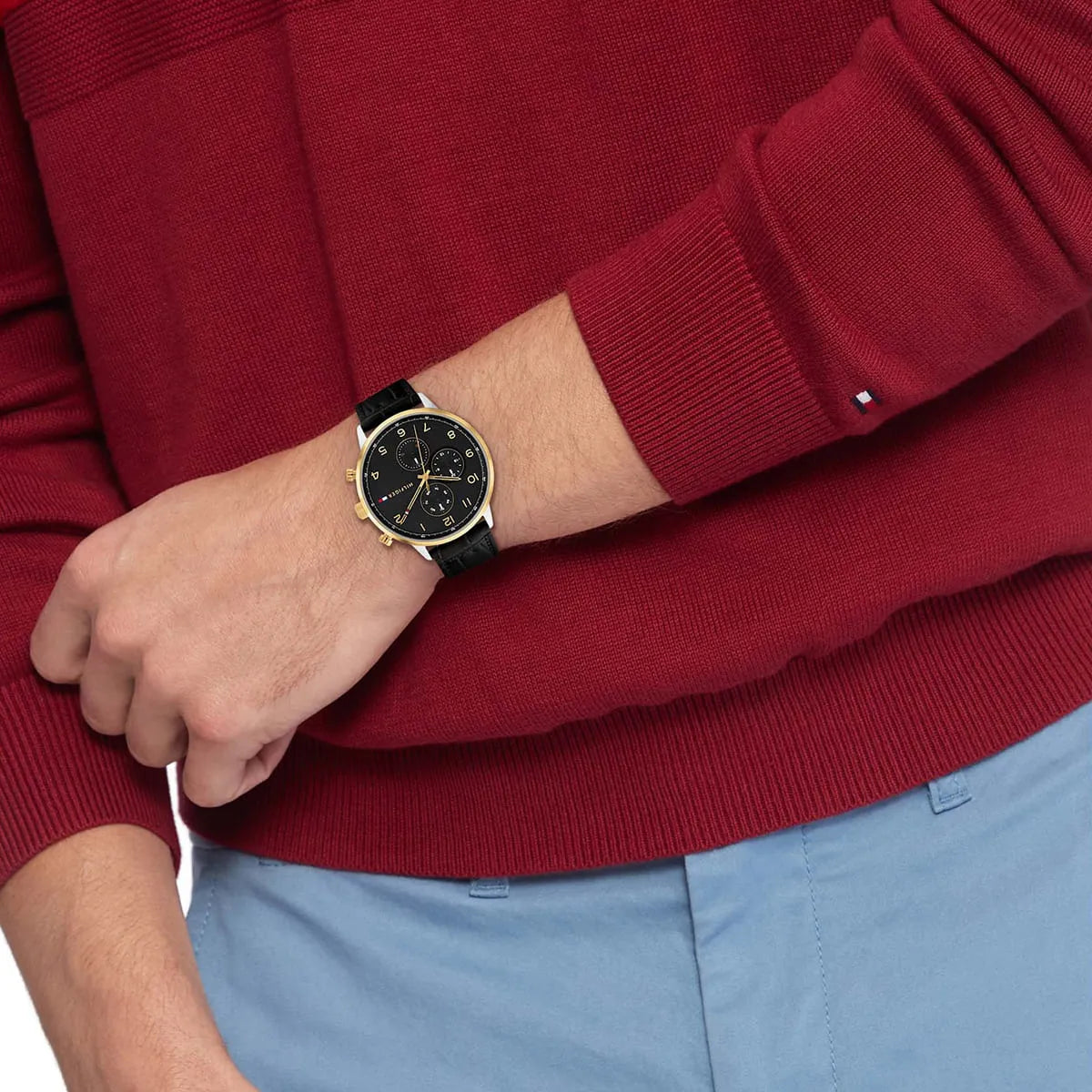 Tommy Hilfiger Leonard watch on wrist with red sweater and blue pants, displaying watch styling
