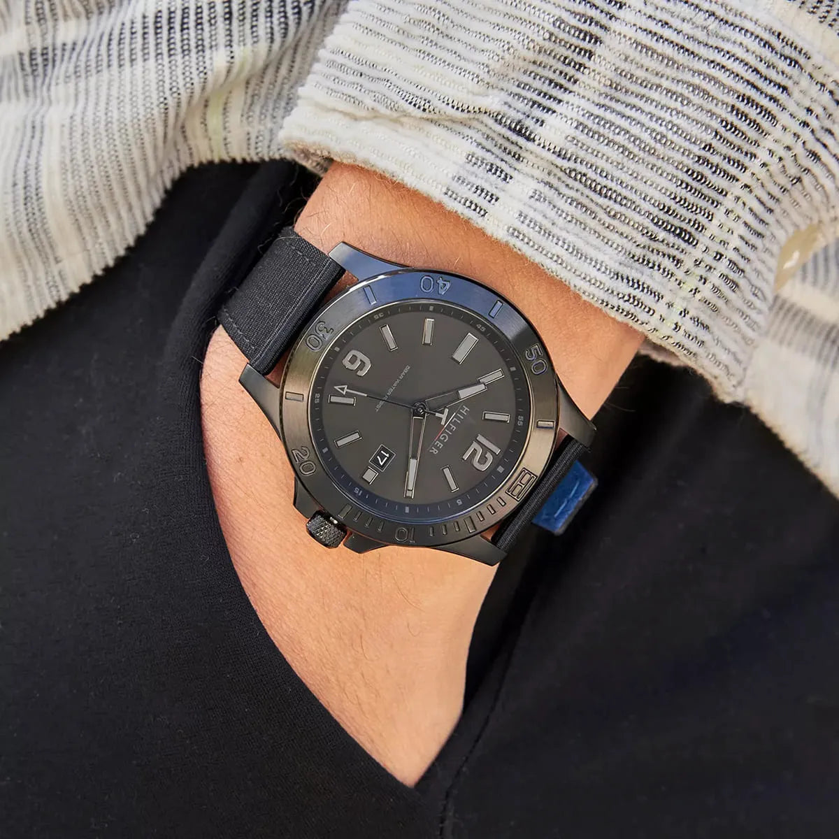 Men's Tommy Hilfiger watch on wrist, lifestyle shot showing black dial and blue strap