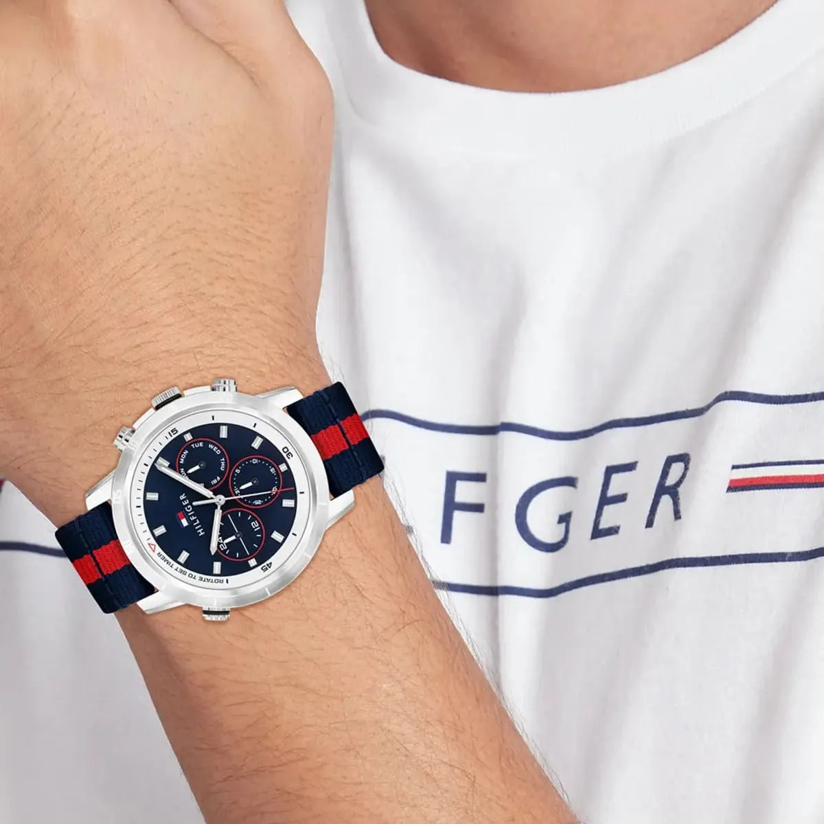 Wrist shot of Tommy Hilfiger chronograph watch on white sleeve with logo visible