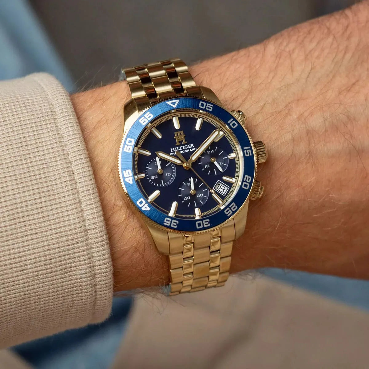 Gold chronograph watch with blue dial worn on man's wrist showing dial and bracelet