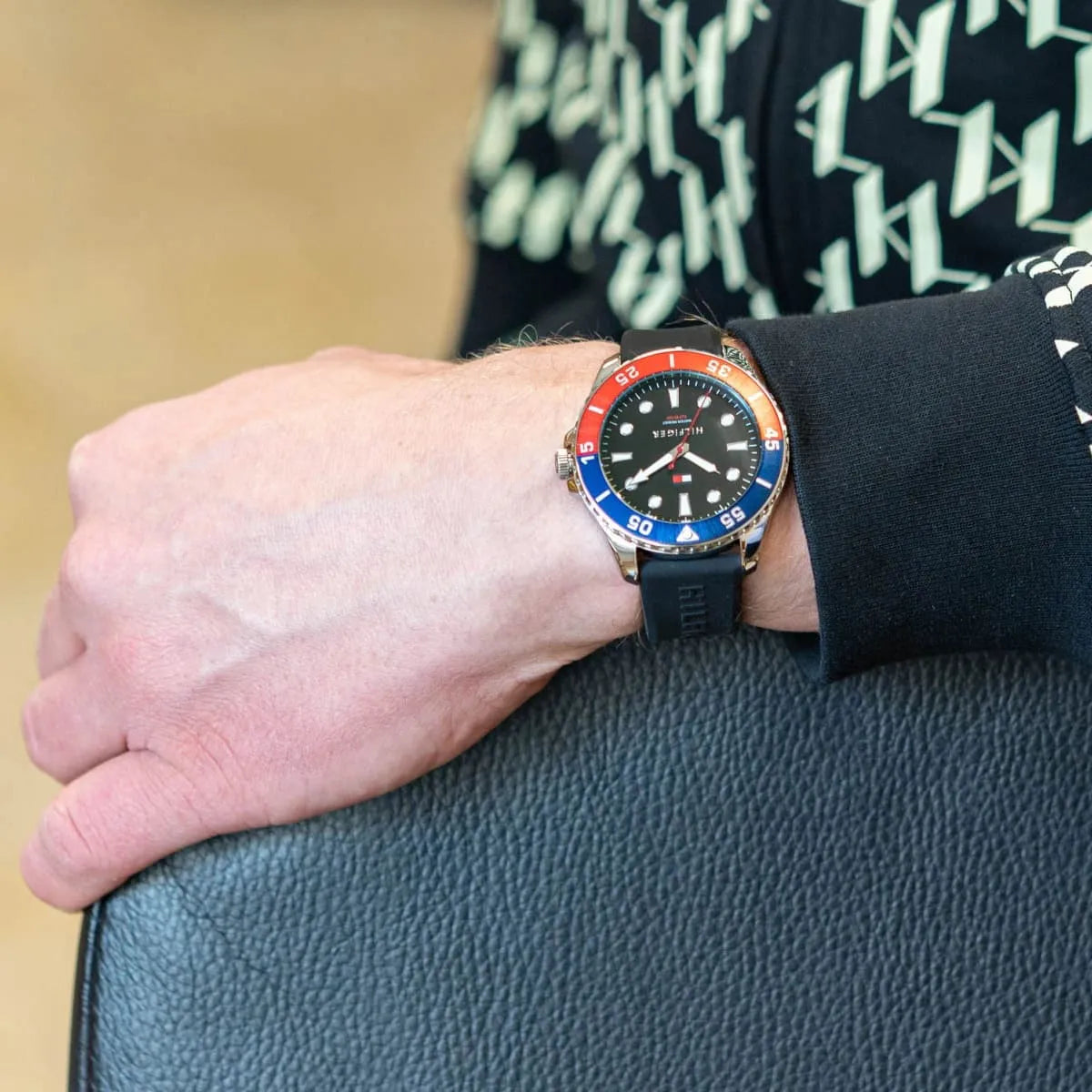Tommy Hilfiger watch worn on wrist showing black dial and blue-red bezel