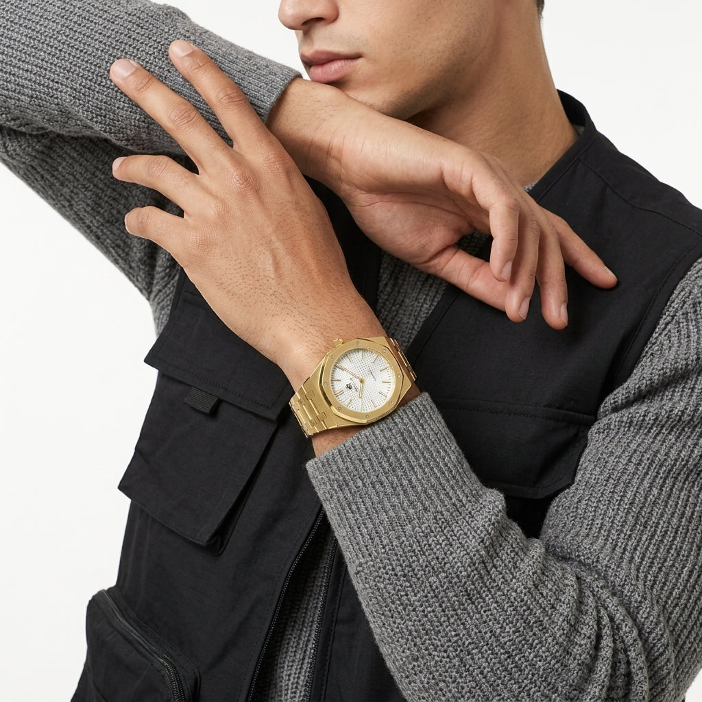 A close-up of a man wearing a gold-tone wristwatch with a white dial, styled over a black utility vest and a gray ribbed sweater.