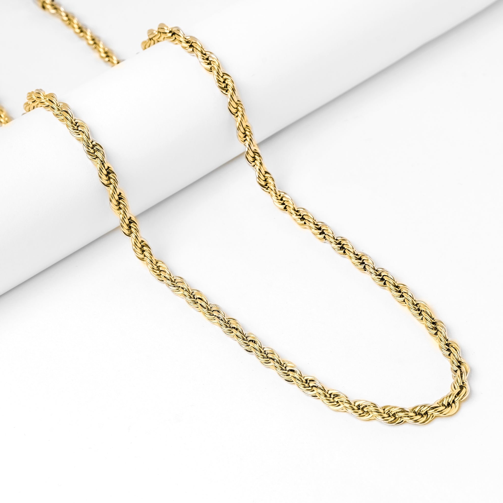 Gold rope chain necklace displayed on white surface