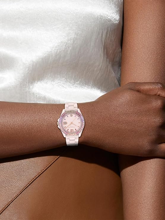 Coach Greyson blush ceramic watch worn on wrist with white top and tan pants