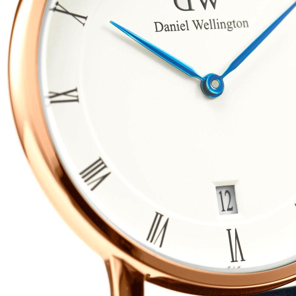 Close-up of white dial with Roman numerals, blue hands, and Daniel Wellington branding