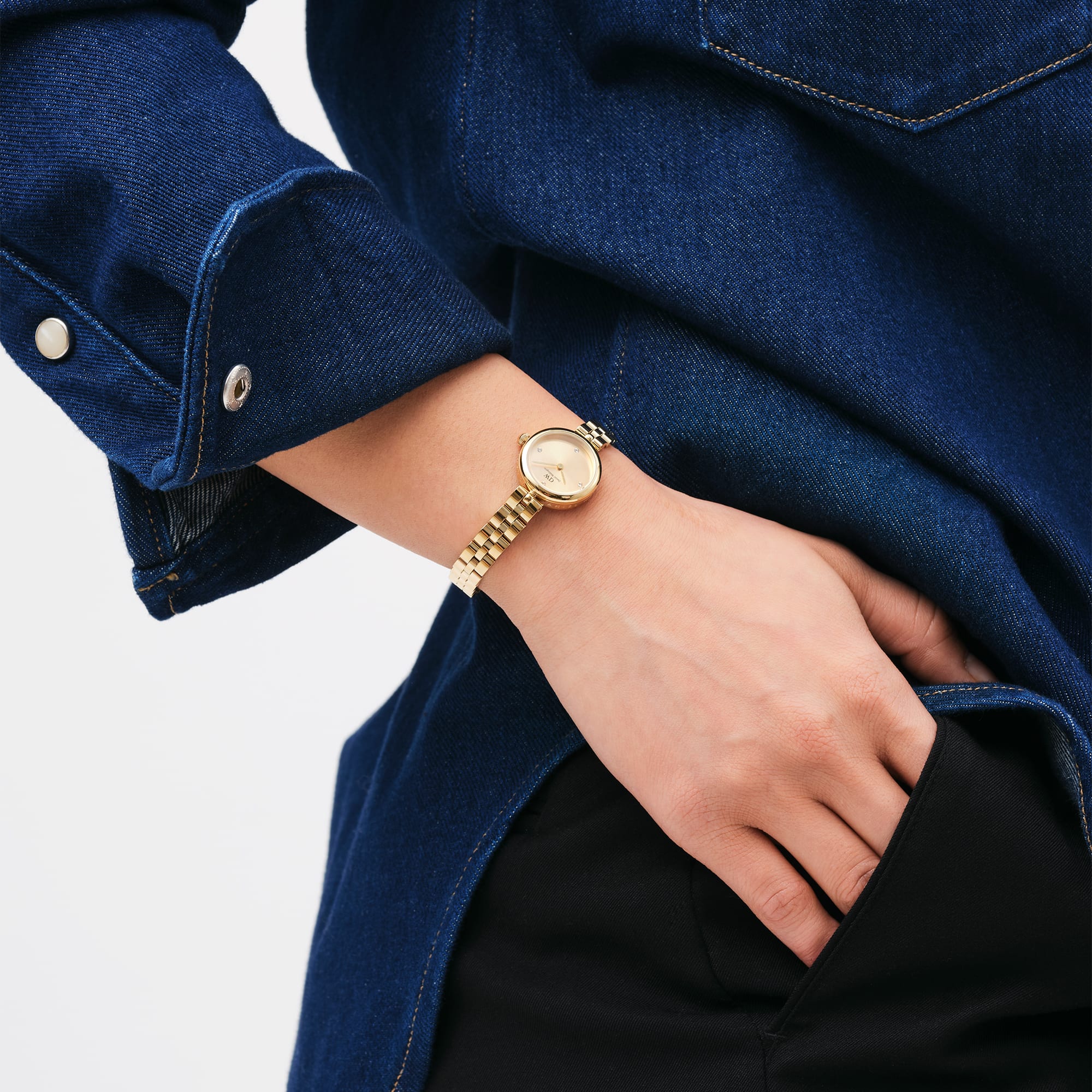 Gold women's watch on wrist with gold link bracelet worn with denim jacket