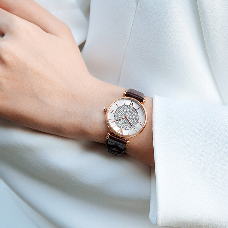 Rose gold watch with crystal pave dial worn on wrist with brown crocodile-embossed leather strap