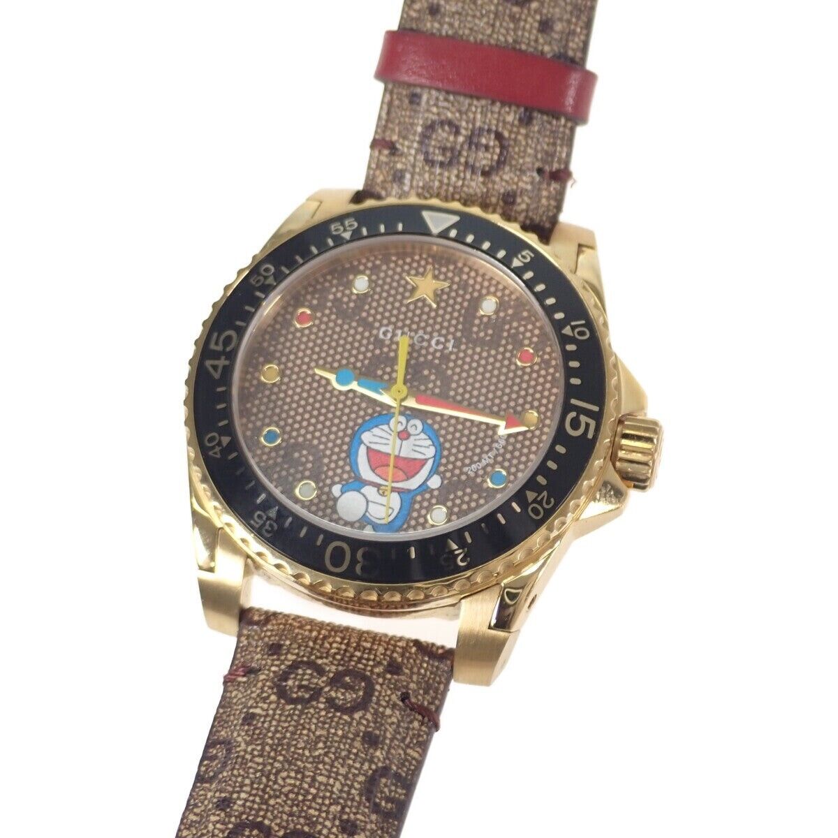 GUCCI Dive Doraemon watch angled view showing gold case and canvas strap with red leather accent