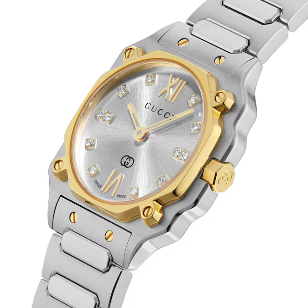 Close-up of GUCCI G-Flat watch dial featuring gold hands, diamond markers, Roman numerals, and interlocking GG logo