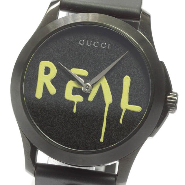 Gucci G Timeless Ghost dial close-up with yellow REAL graphic on black background