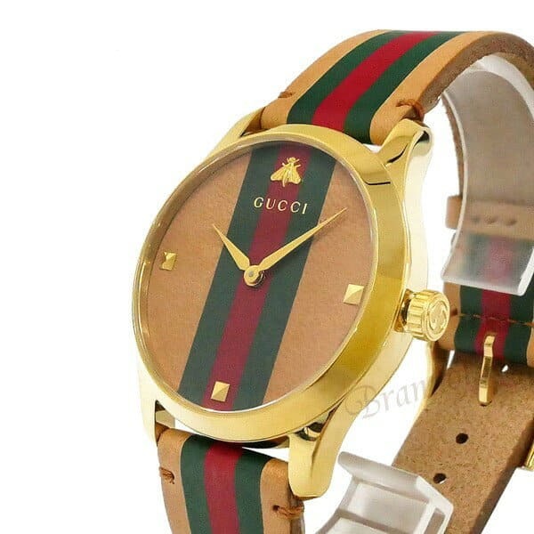 Gucci G-Timeless 38mm watch at angle showing gold case and striped strap
