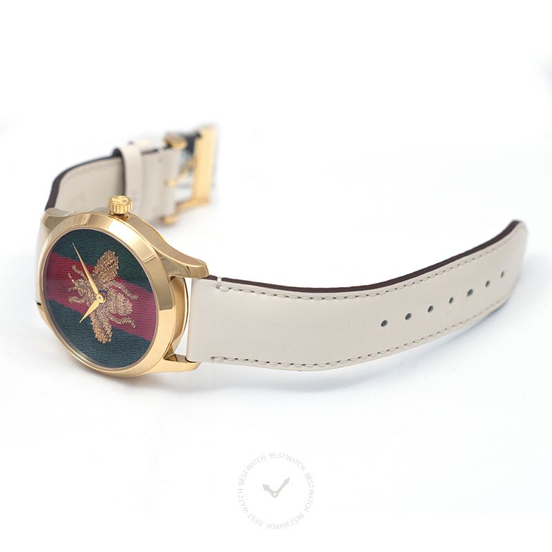 Side angle view of Gucci G-Timeless watch showing gold case, cream strap, and embroidered bee dial
