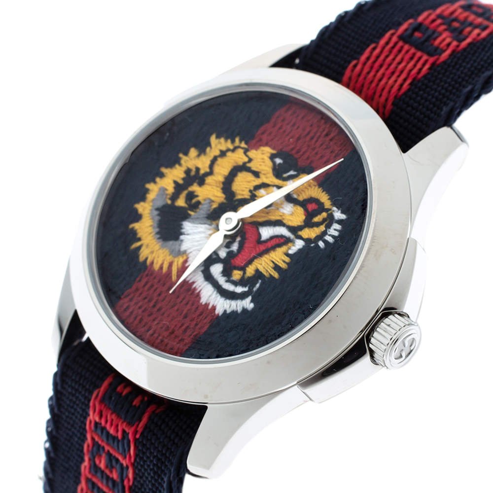 Gucci G Timeless tiger watch angled view showing white case, embroidered dial, and striped strap