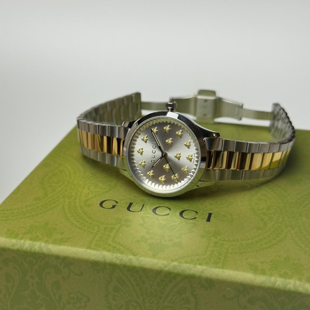 Gucci G-Timeless watch displayed on green Gucci branded box, showing dial and two-tone bracelet
