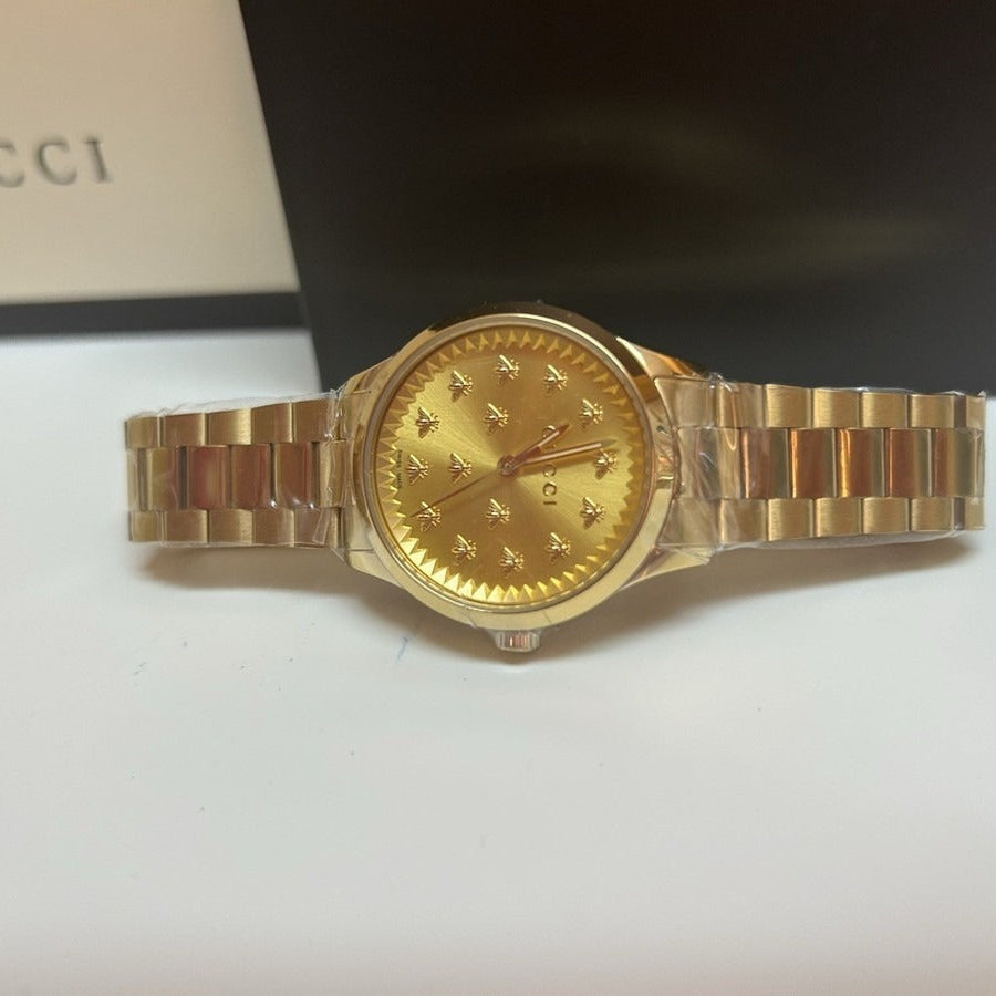 Gucci G-Timeless gold plated watch worn on wrist with gold bracelet