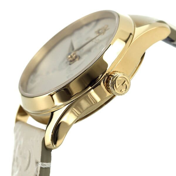 Gucci G-Timeless watch three-quarter view showing gold case, white dial, and leather strap