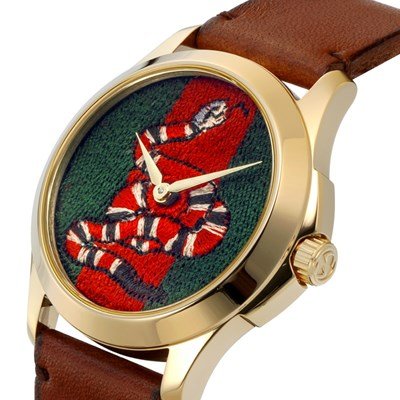 Three-quarter angle view of Gucci snake watch with gold-tone case and brown leather