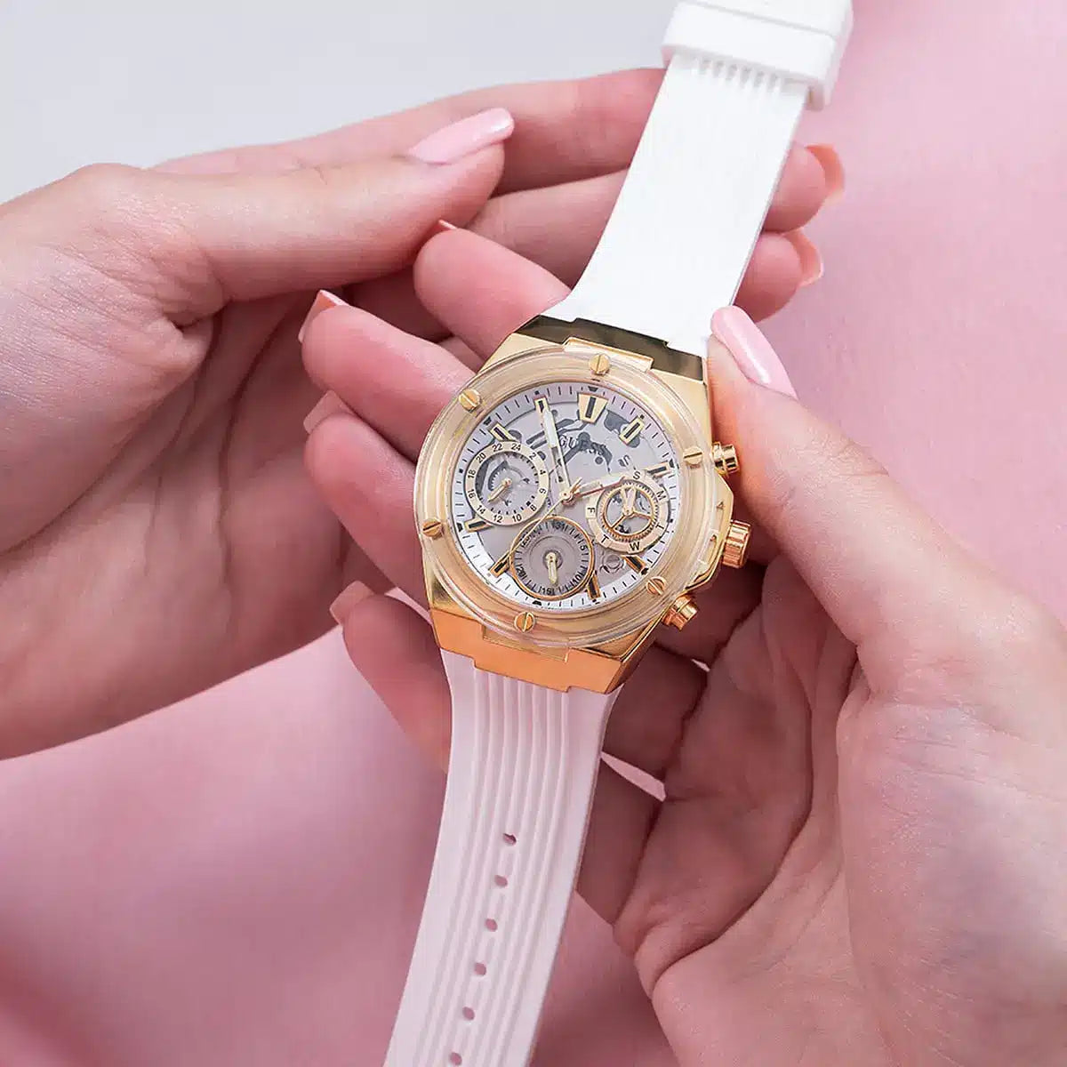 Guess GW0409L2 gold chronograph watch with white rubber strap held in hand on pink background