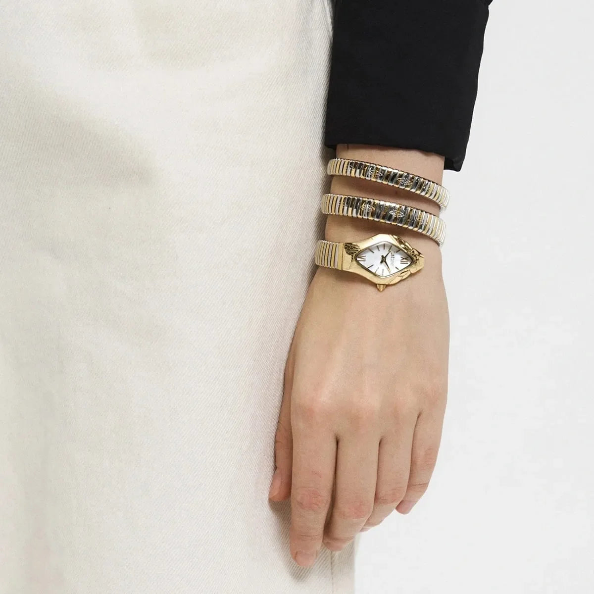 Watch styled on wrist with cream and black clothing, displaying gold and silver snake bracelet design
