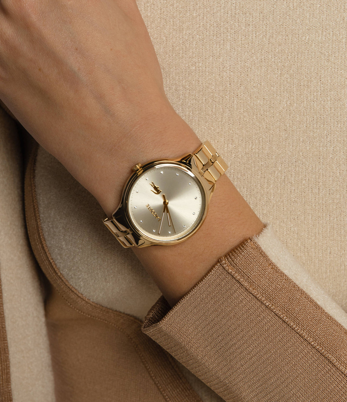 Lacoste gold watch worn on wrist with neutral toned clothing