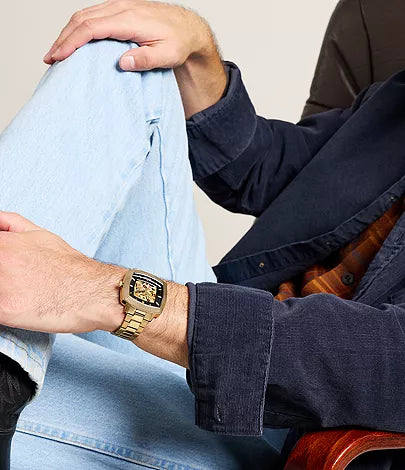 Gold-tone skeleton dial watch styled on-wrist with blue shirt and jacket