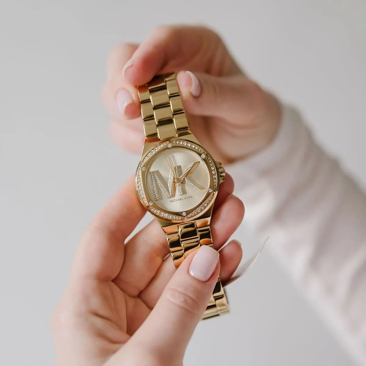 Lennox gold-tone watch held in hand showing crystal bezel and MK logo dial