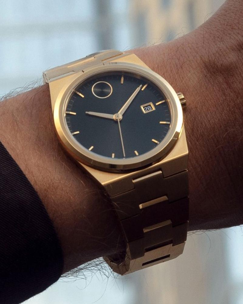 Movado BOLD Quest men's watch worn on wrist with gold-tone case and bracelet