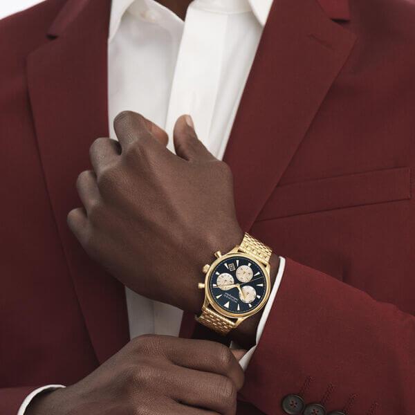 Movado Heritage chronograph watch worn on wrist with gold case and black dial