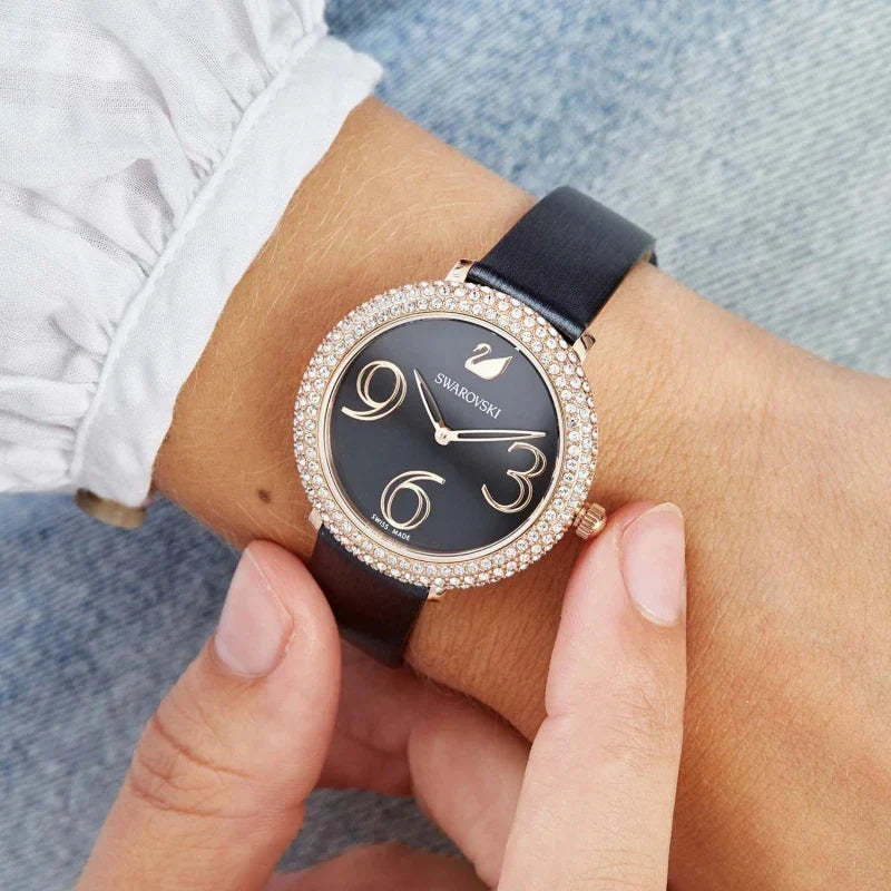 Swarovski women's watch worn on wrist, showing crystal bezel, black dial, and black leather strap