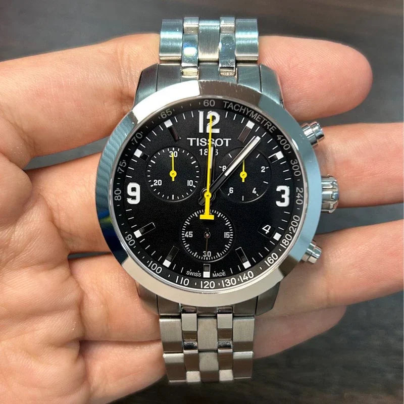 Tissot PRC 200 chronograph watch held in hand showing black dial with tachymeter scale and yellow accents