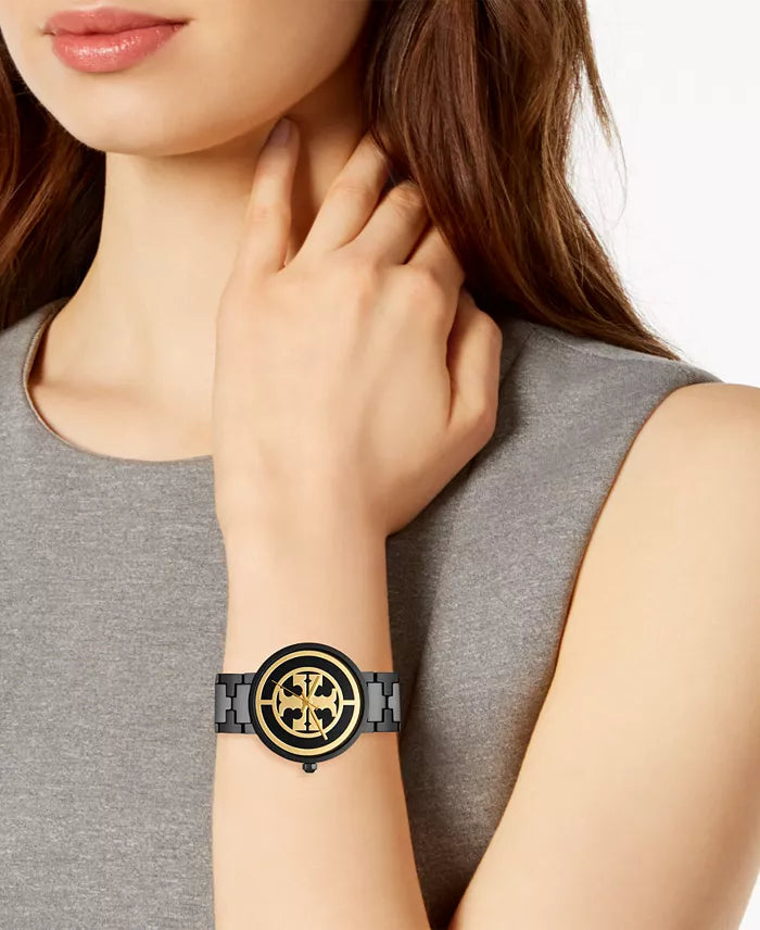 Tory Burch Reva watch worn on wrist, displaying black case with gold logo dial and black bracelet