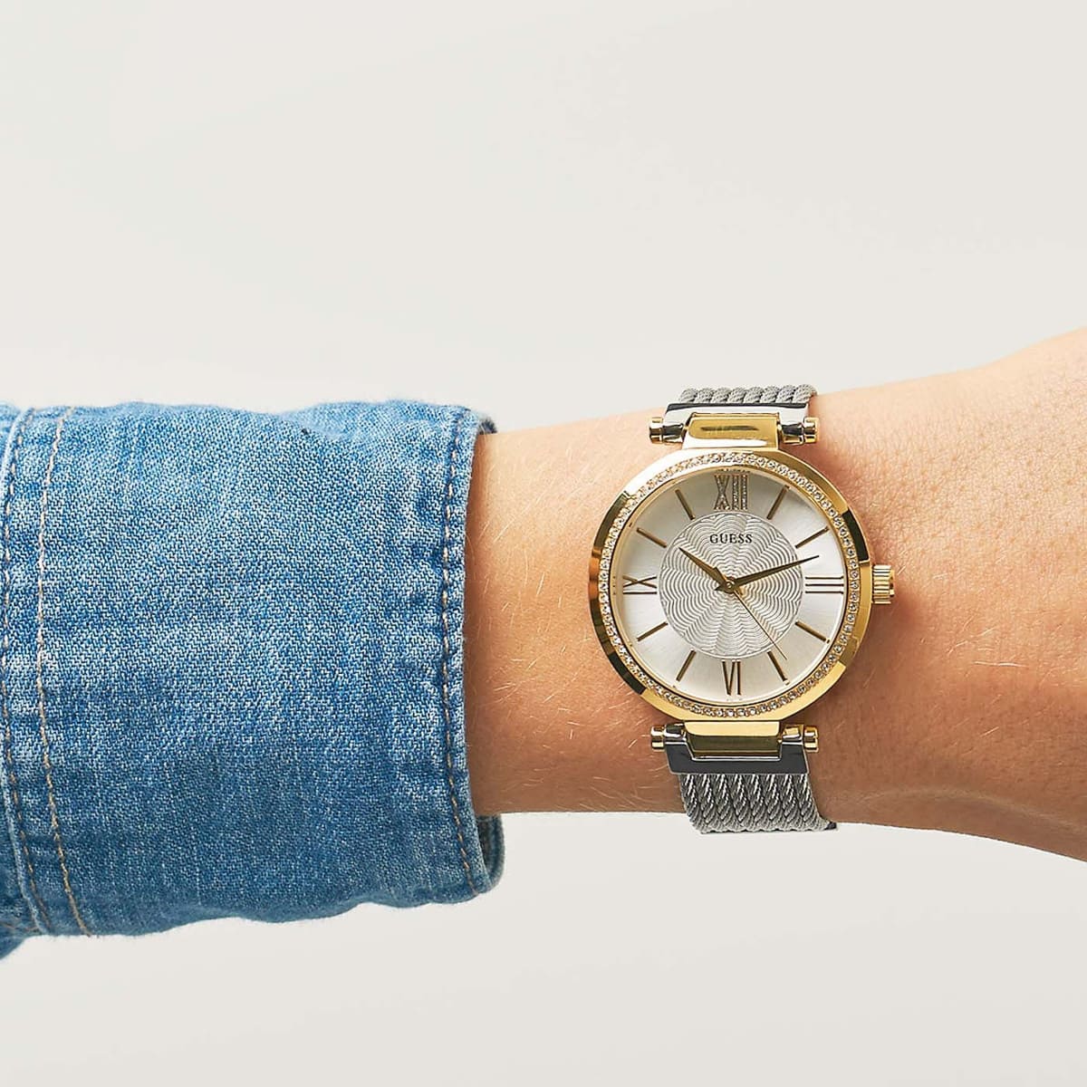 Guess Soho women's watch worn on wrist with denim sleeve, displaying gold and silver design