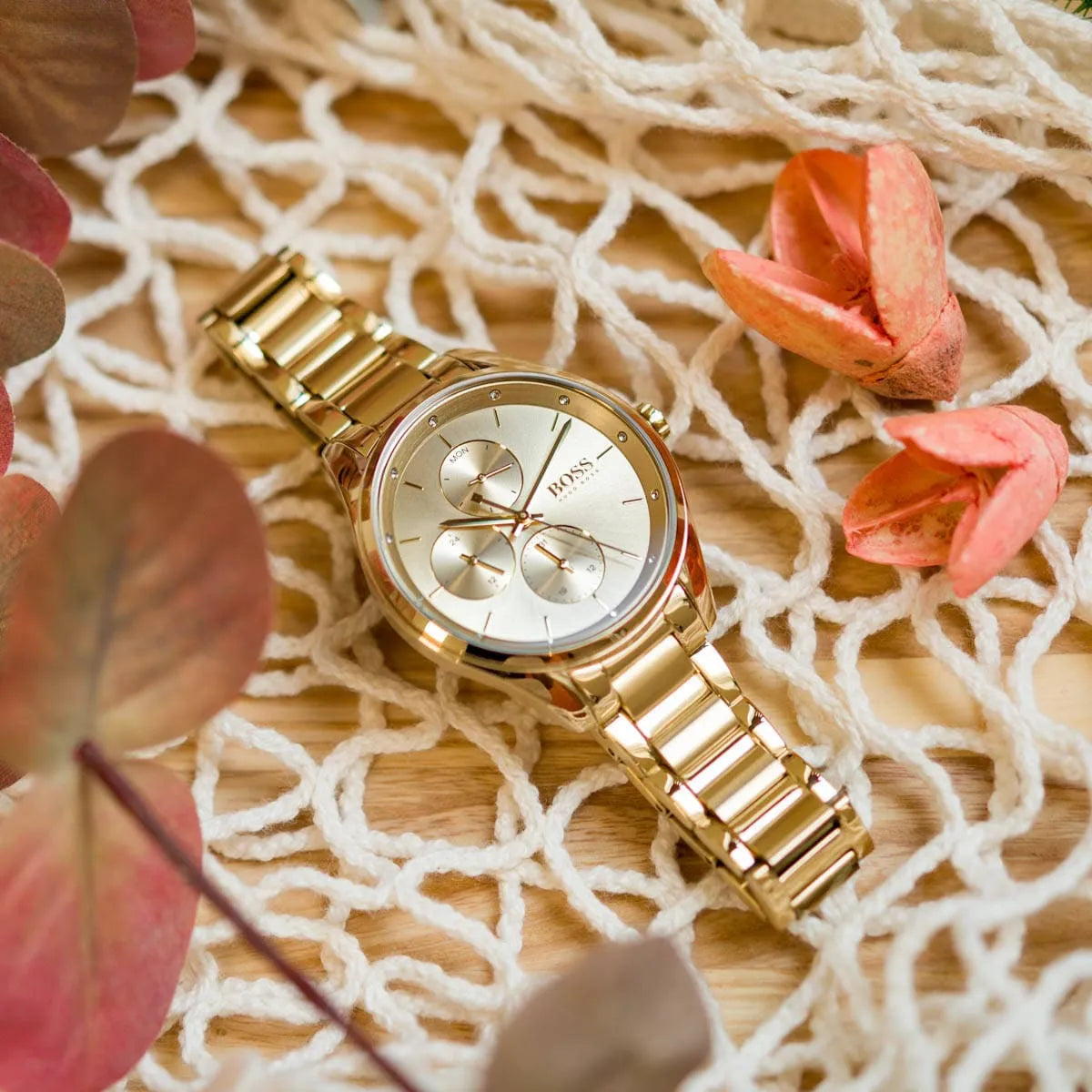 Hugo Boss Grand Course gold watch with gold steel strap displayed on decorative netting
