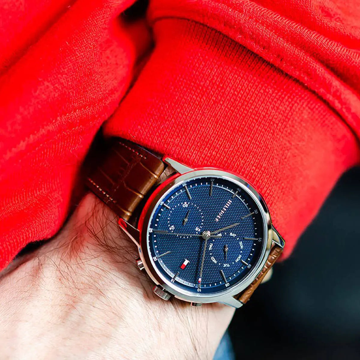 Watch on wrist with red sleeve showing navy dial and chronograph details