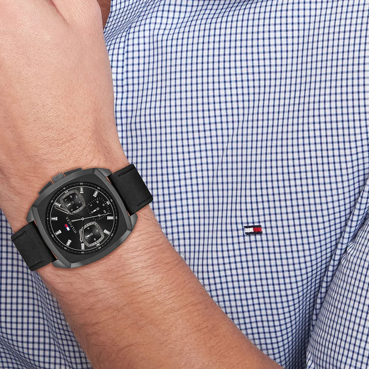 Tommy Hilfiger black leather strap watch worn on wrist with blue checkered shirt