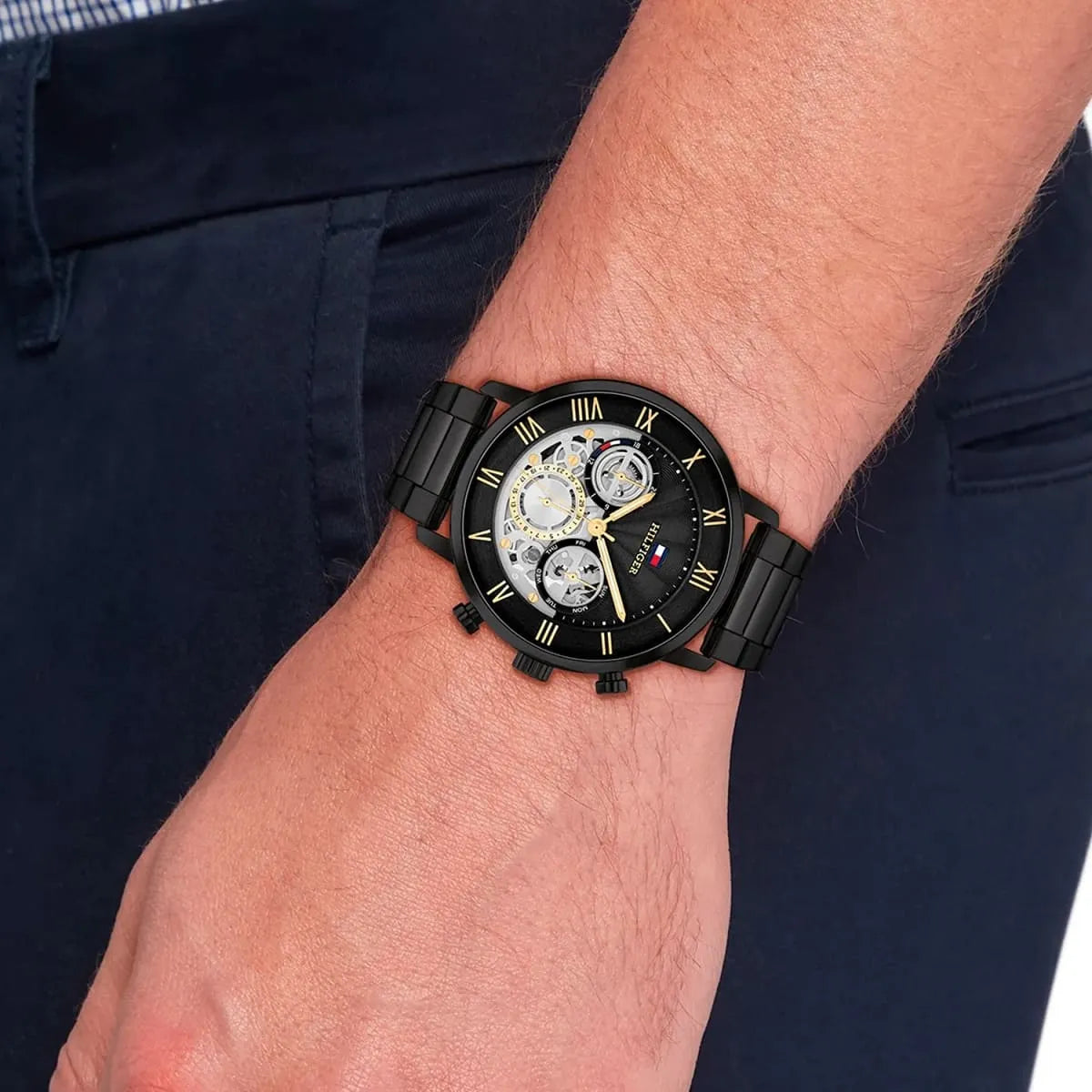 Tommy Hilfiger black steel watch worn on wrist with navy pants