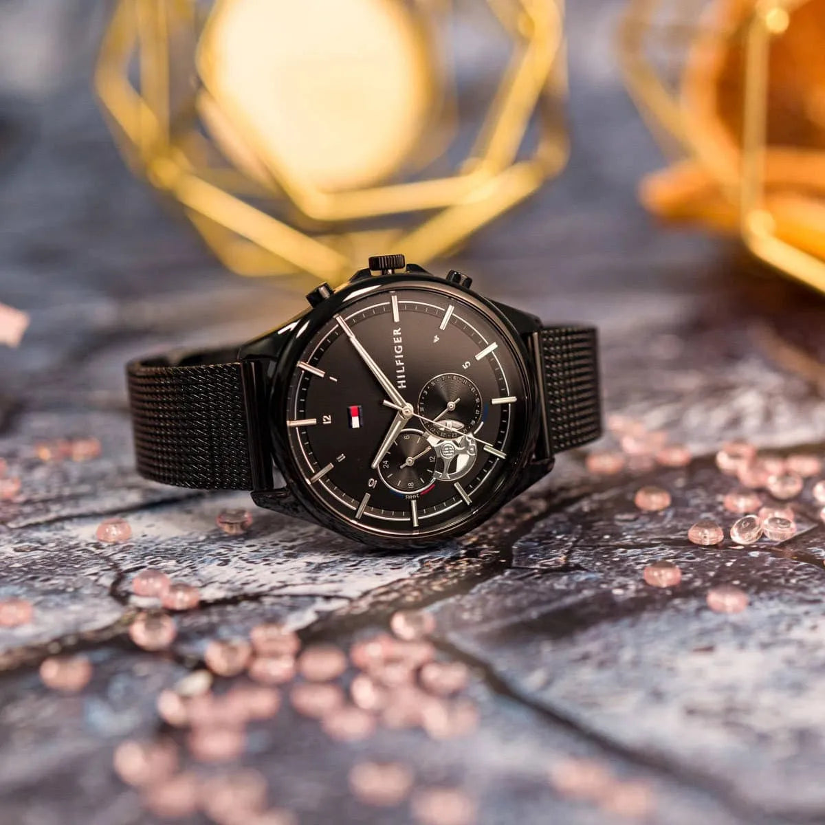 Tommy Hilfiger Quinn black watch with mesh strap displayed on decorative surface