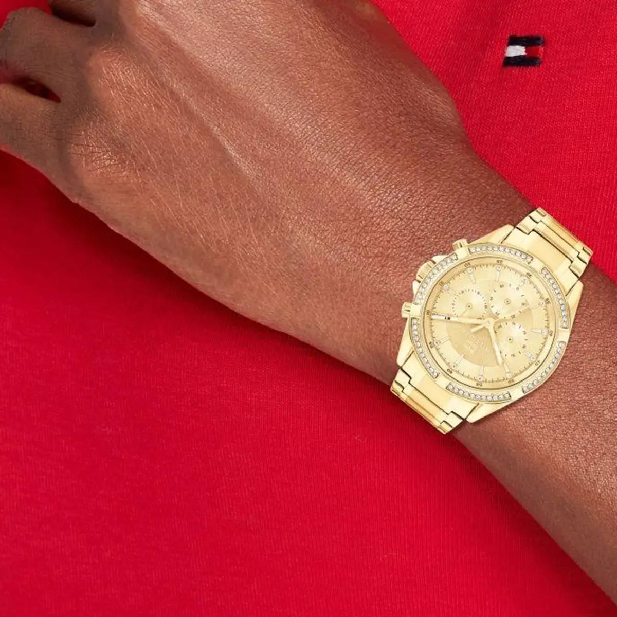 Tommy Hilfiger gold women's watch on wrist against red fabric background