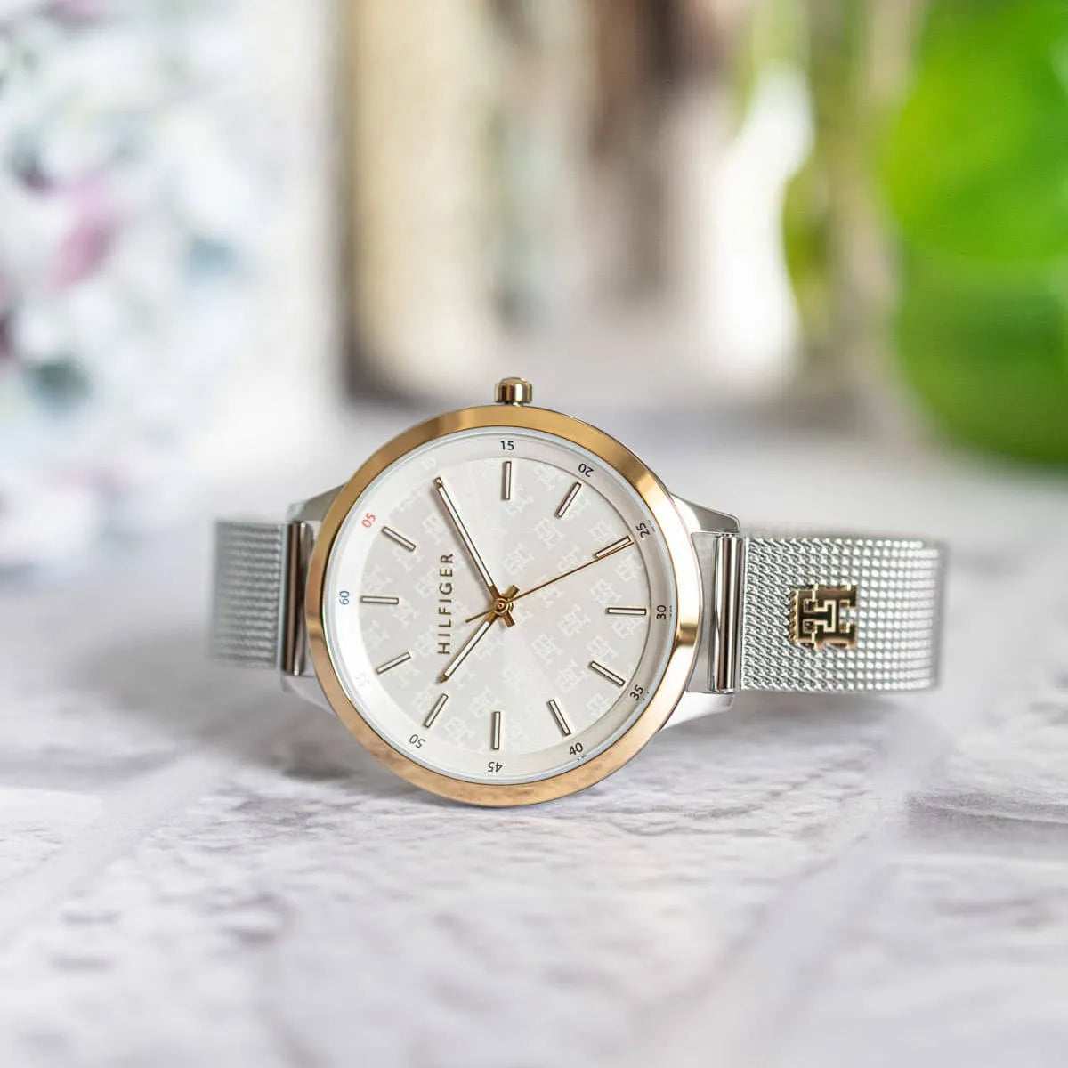 Tommy Hilfiger Iris watch flat lay on surface with white dial and silver mesh band