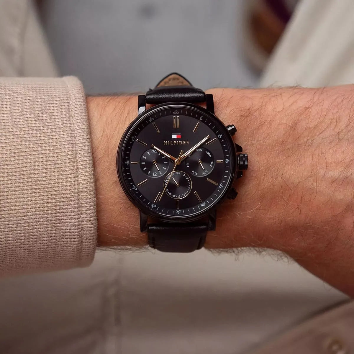 Tommy Hilfiger TYSON men's watch on wrist displaying black chronograph dial with gold accents and leather band