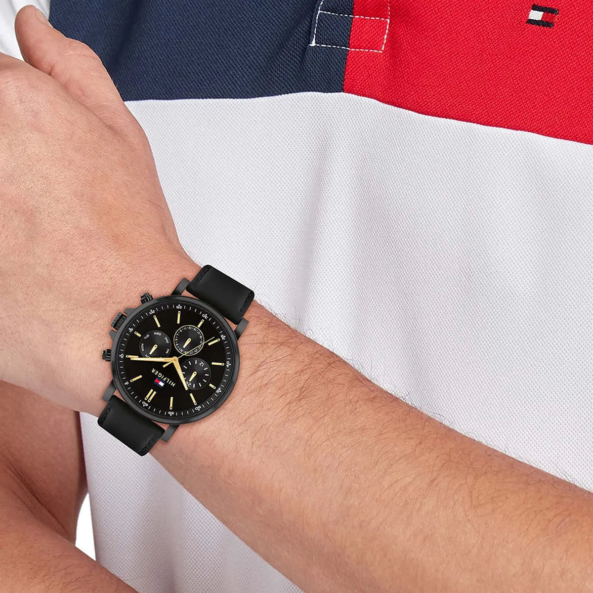 Tommy Hilfiger TYSON black chronograph watch worn on wrist with Tommy Hilfiger flag background