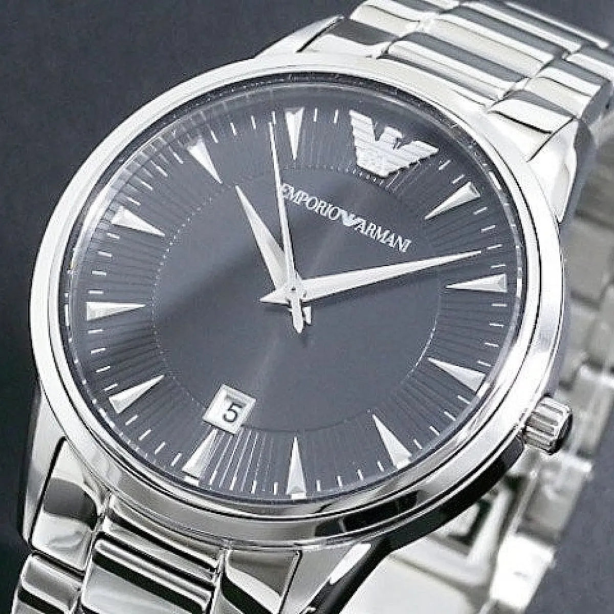 Close-up of black dial showing Emporio Armani branding, index markers, white hands, and date display