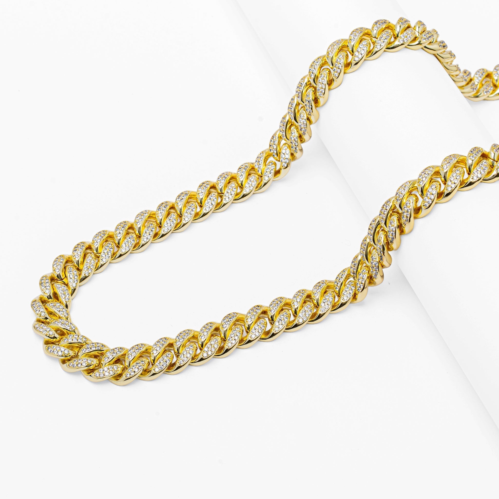 Gold 8mm cuban link chain with crystal embellishments draped on white background